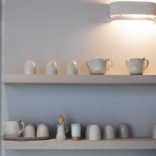 Speckled ceramic teacups and teapots lined on a wall shelf