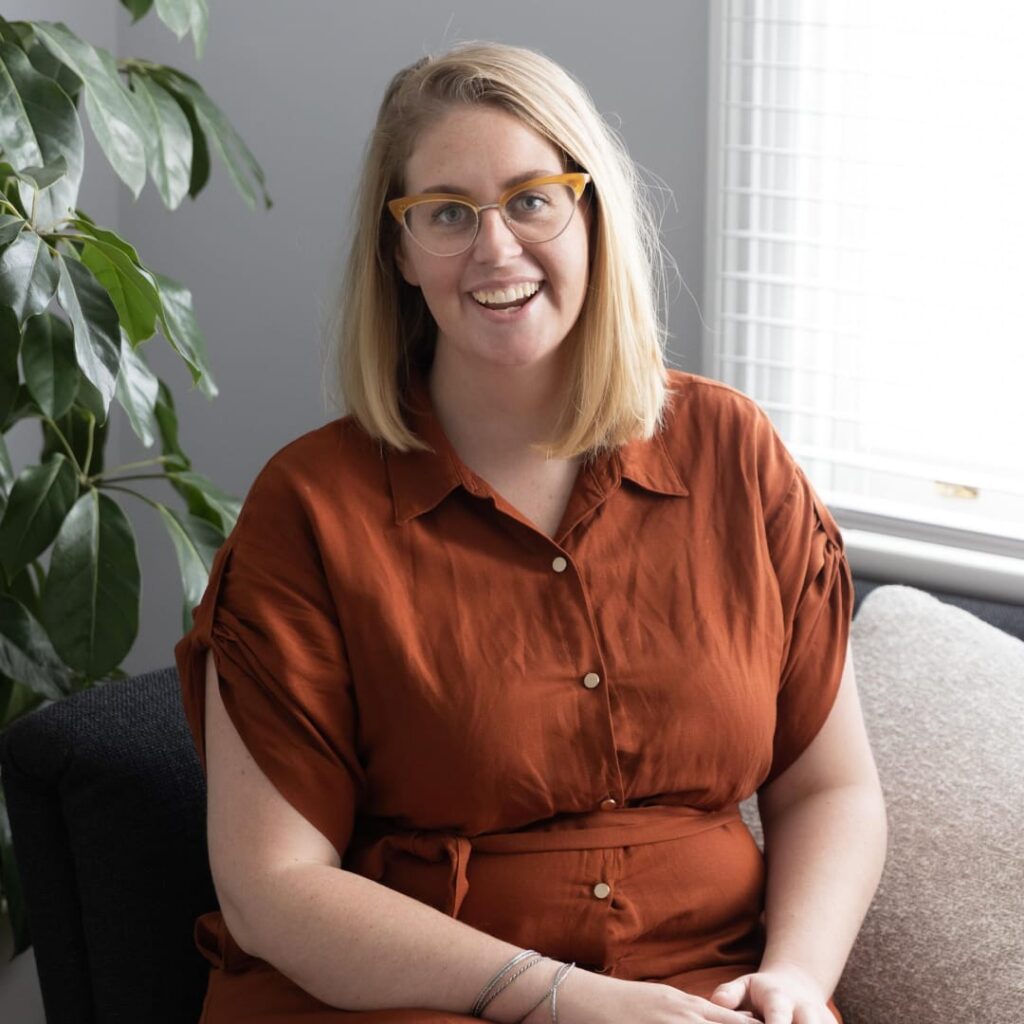 Courtney Tanner in orange dress sitting on a sofa