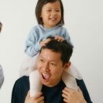 a smiling dad with a toddler sitting on his shoulder