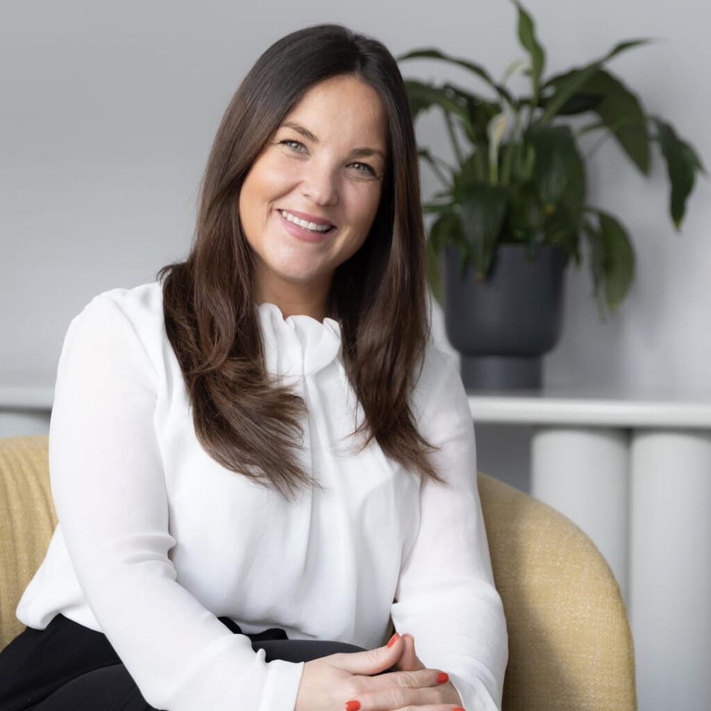 Jen Harris in a white blouse sitting on a sofa