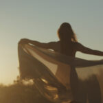 Woman standing while spreading a scarf in the middle of a open air field