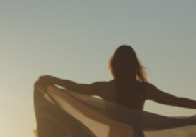 Woman standing while spreading a scarf in the middle of a open air field
