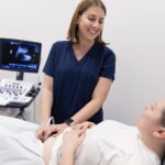 A clinician sitting down performing ultrasound scan to a client