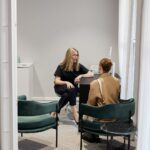 Doctor Rachael Knight is sitting on an office chair, giving a consultation to a client inside a consultation room