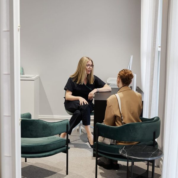 Doctor Rachael Knight is sitting on an office chair, giving a consultation to a client inside a consultation room